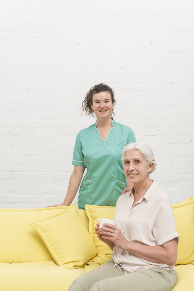 smiling-senior-woman-sitting-sofa-holding-coffee-cup-front-nurse_23-2147861584